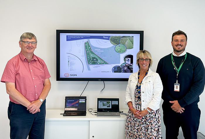 An image with three people posing for camera standing near a monitor