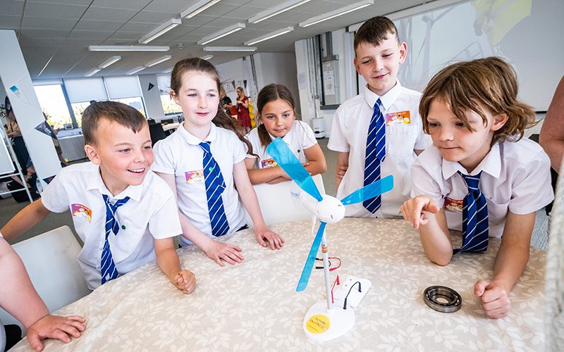 Young school children gathered around a model wind turbine