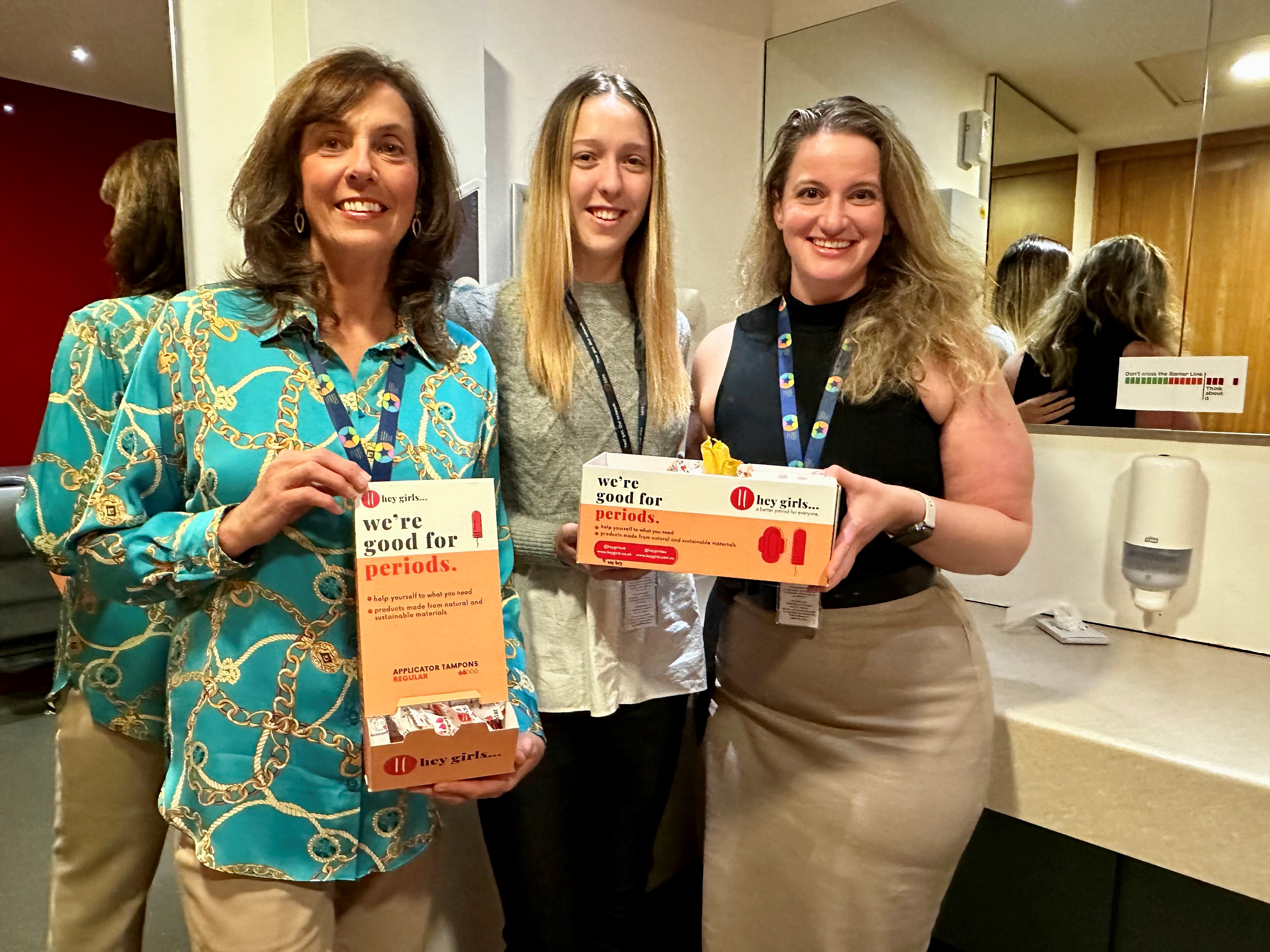 Three women holding boxes of Hey Girls period products