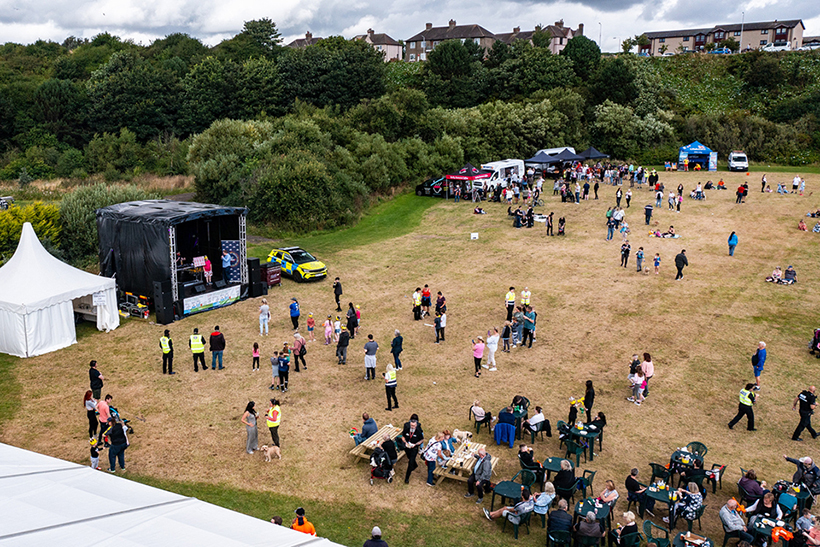 Drone view of a crowd of people gathered in park, with a marquees, tents and a stage