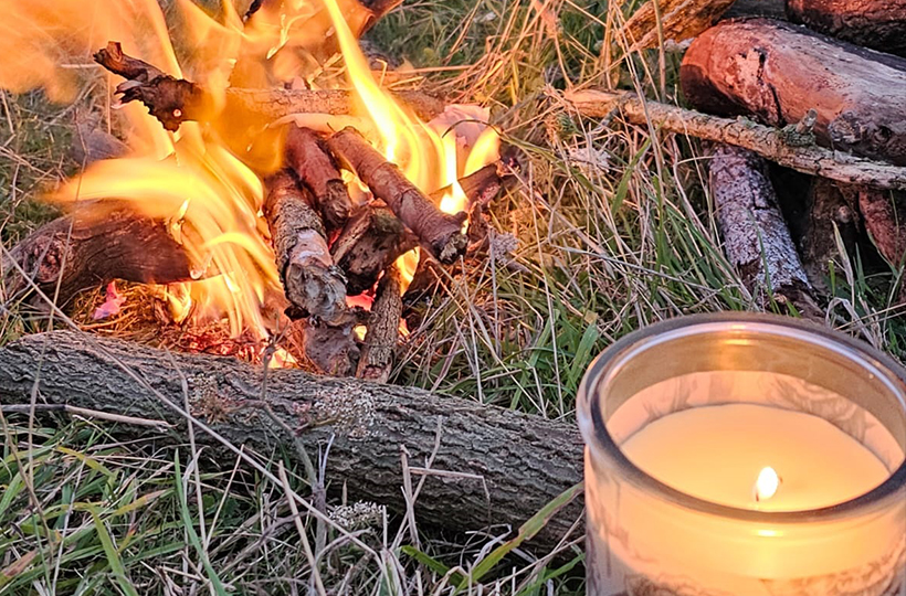 A candle lit beside a campfire