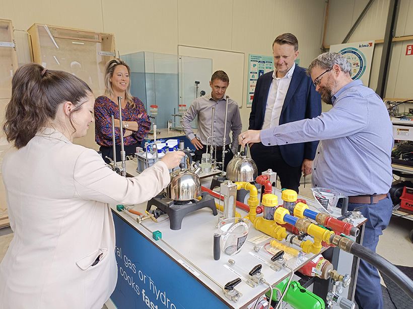 Five people gathered around a table with lots of pipes and equipment on it