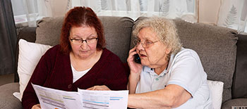 Two women sitting on a sofa looking at information on a leaflet. One woman is making a phone call. 