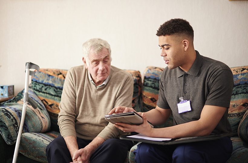 young man wearing lanyard talking to elderly man and showing him a leaflet