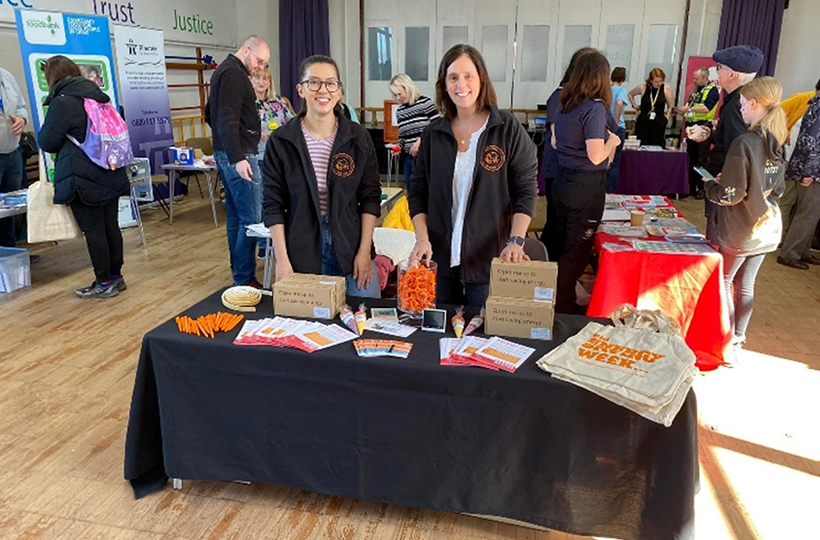 2 women from Better Housing Better Health standing behind a table set up with information