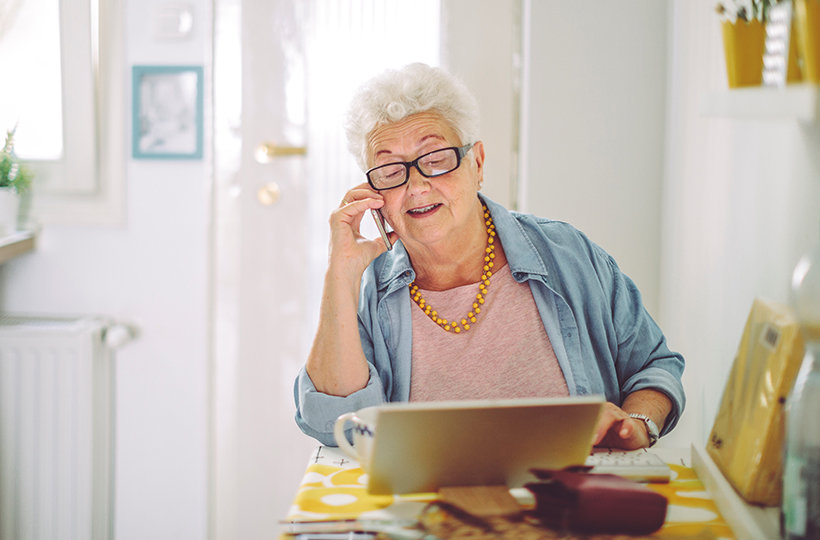 elderly lady looking at paperwork and making a phone call in her home