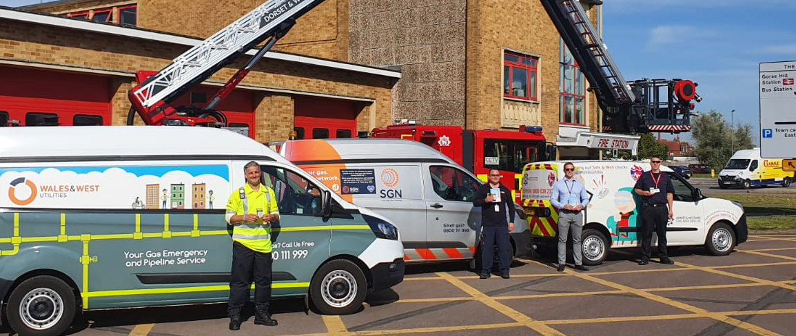 image showing 3 vans and engineers from gas distribution networks outside a firestation with a fire engine in the backgroun. 