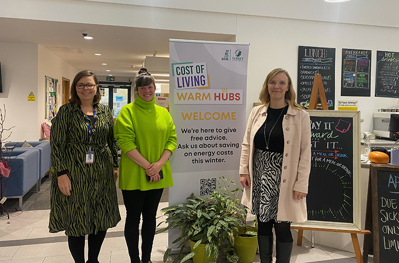 3 women stand next to a display banner showing Surrey Warm Hub services