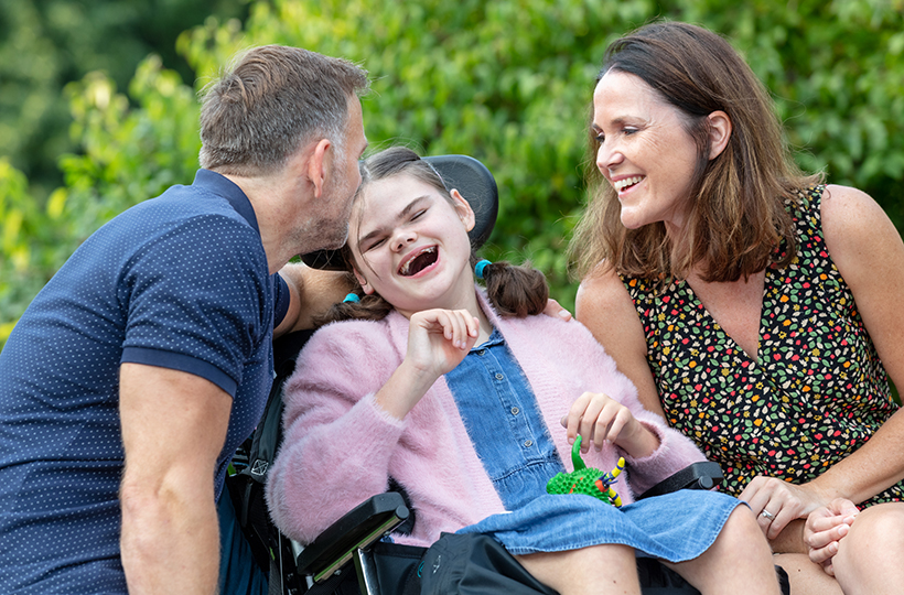 A man and a woman smiling and laughing with a young girl in a wheelchair