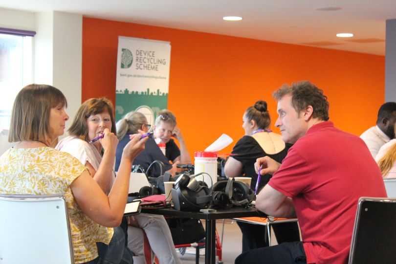 A group of Digital Kent service users sitting round a table with IT equipment in the middle of it