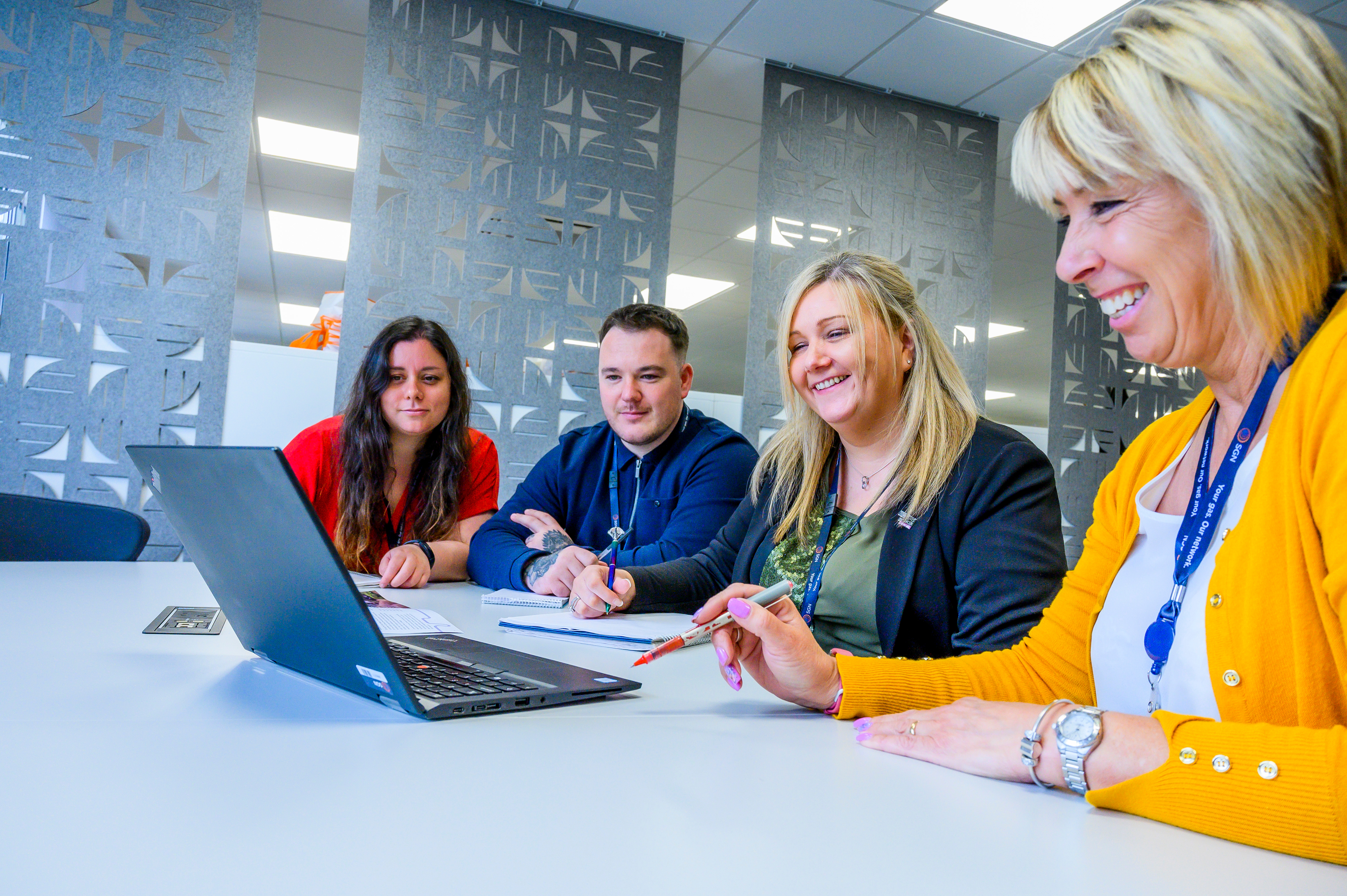 Four smiling people sat around a laptop
