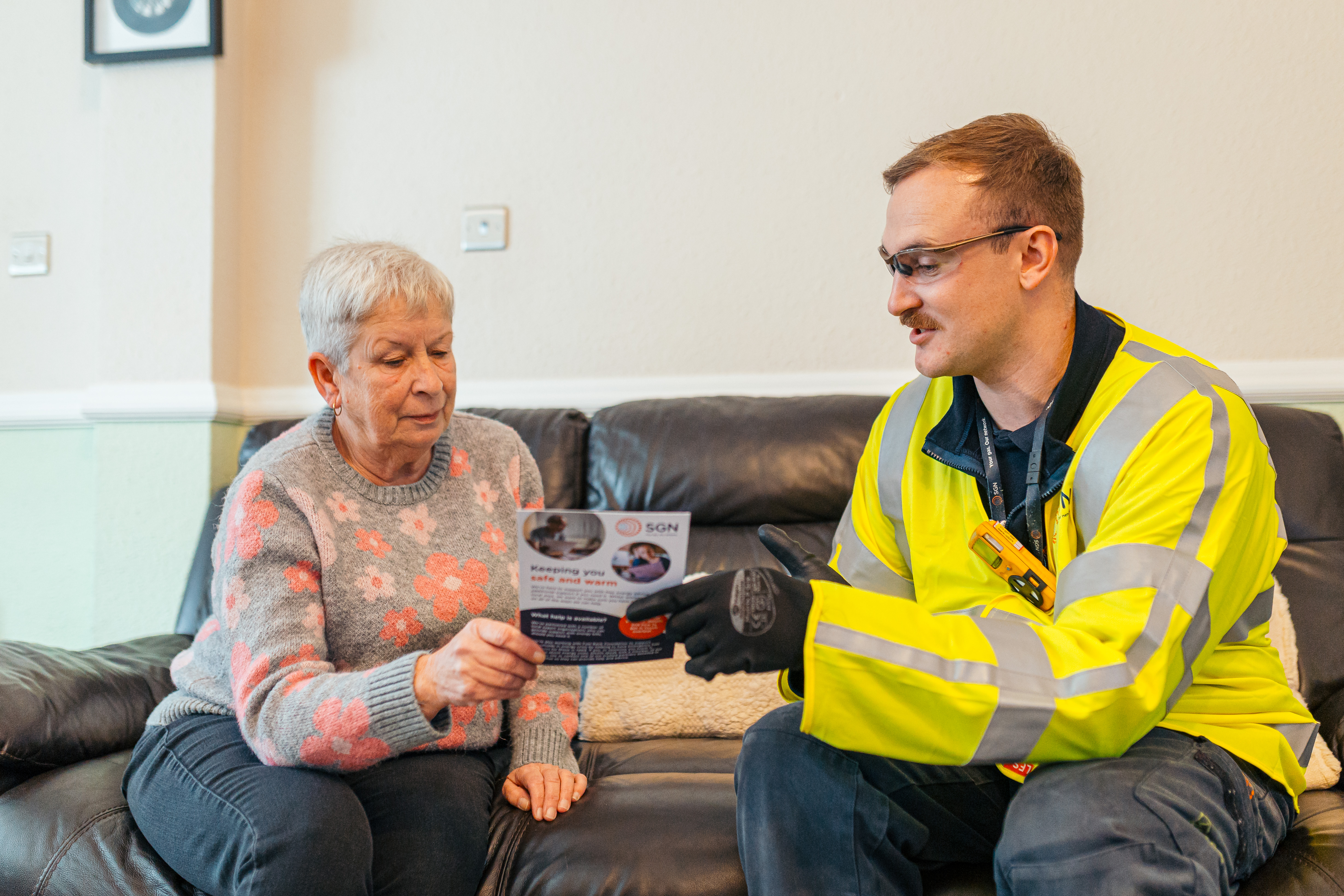 An older woman and SGN engineer sat on a sofa with a leaflet