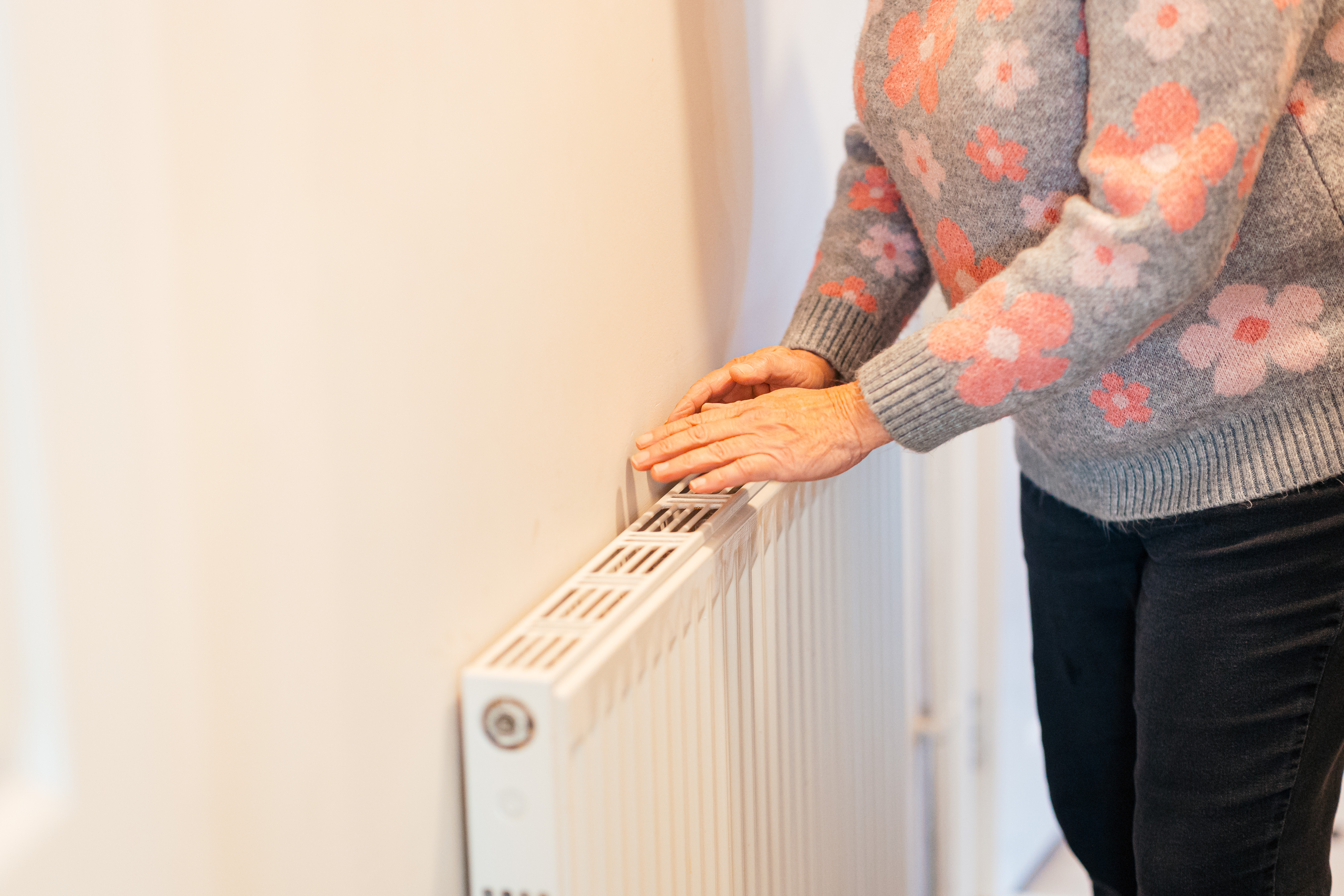An older woman warming her hands on a radiator