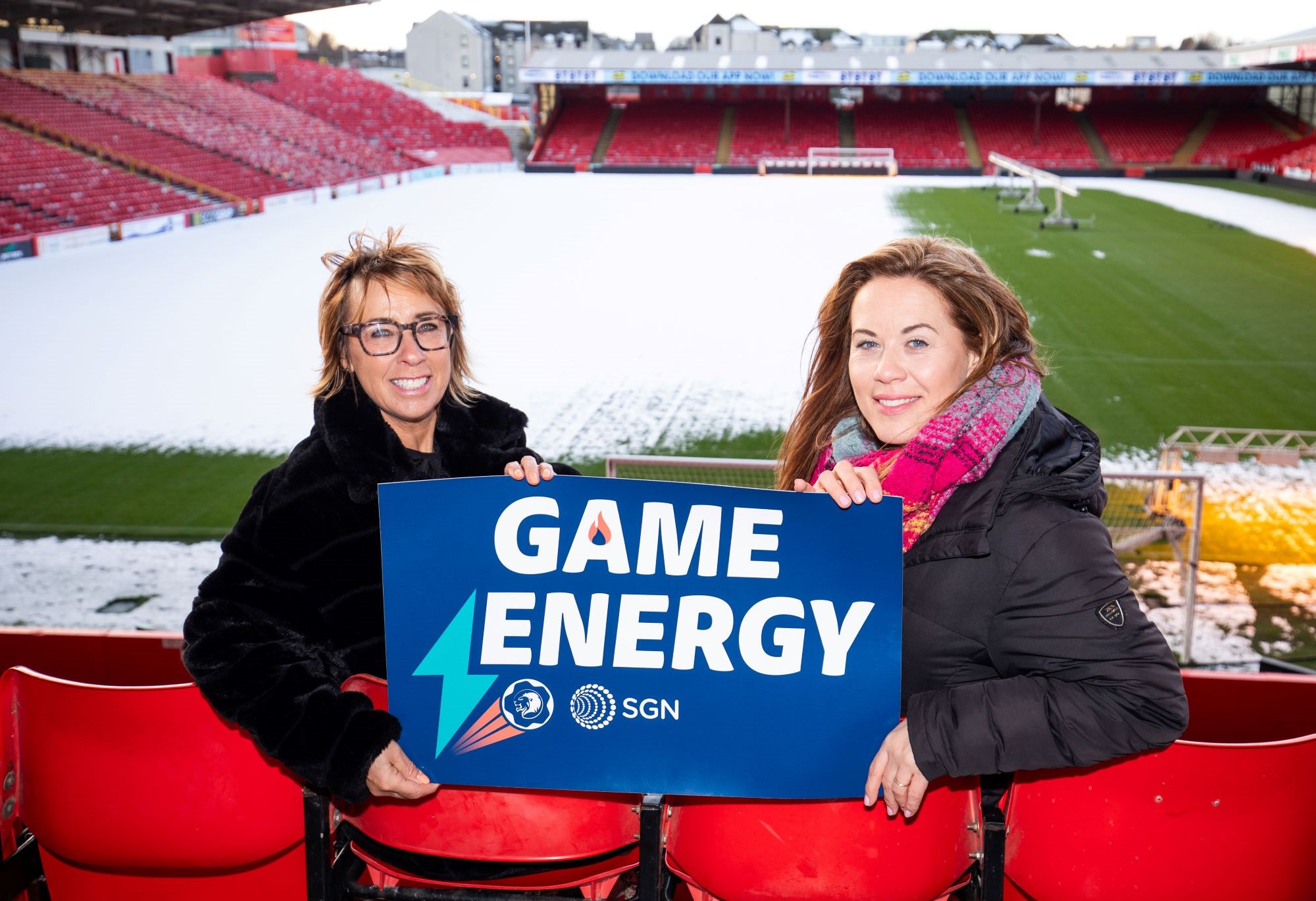 Members of the SGN and SPFL Trust teams are sitting in the stands of a snowy football stadium, holding a SGN-branded banner that says 'Game Energy'