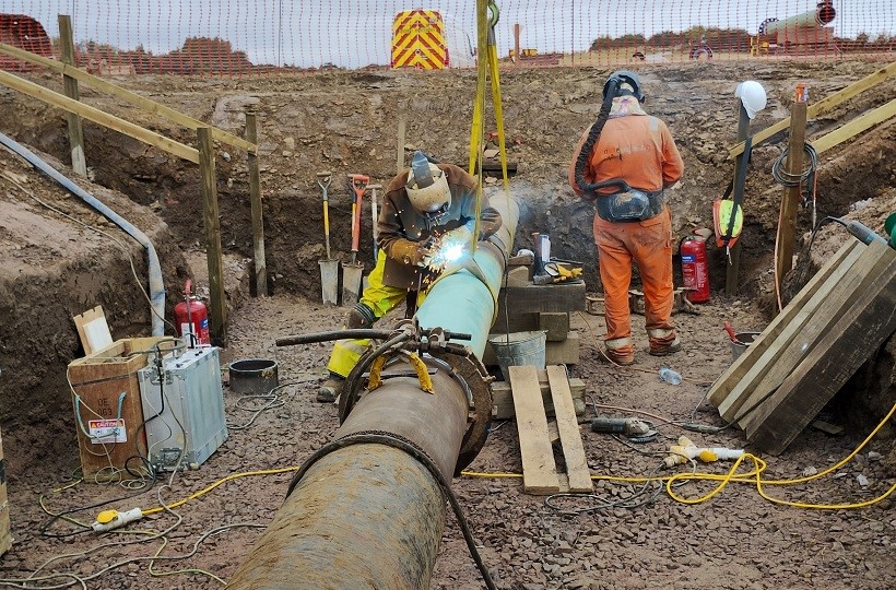 Gas engineers at work in field on large high pressure pipeline.