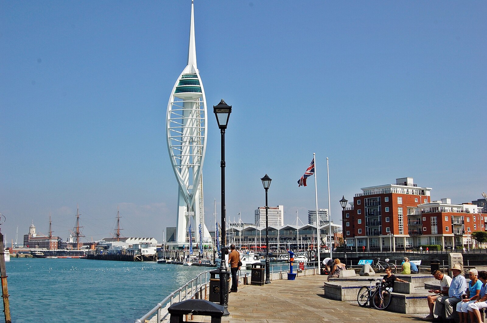 On a sunny day, people gather on the Portsmouth waterfront. In the background there is a slender viewing tower.