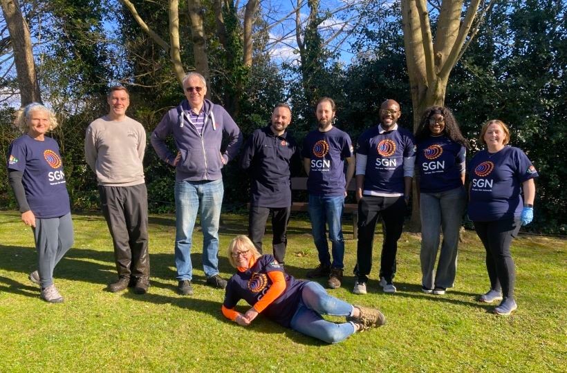 A group of smiling people stood on grass in front of trees
