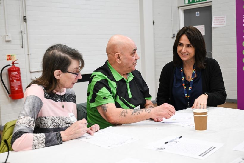 Janet, a female member of staff from SGN, sits next to two older people - one male and one female - to discuss dementia issues.