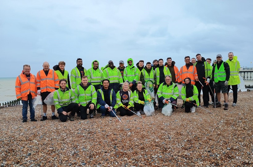 A large group of people in SGN PPE armed with litter pickers and bags on a stony beach in Worthing