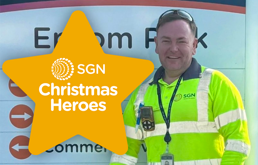 A smiling man in PPE in front of the entrance to our Epsom depot with a star that says 'SGN Christmas Heroes'
