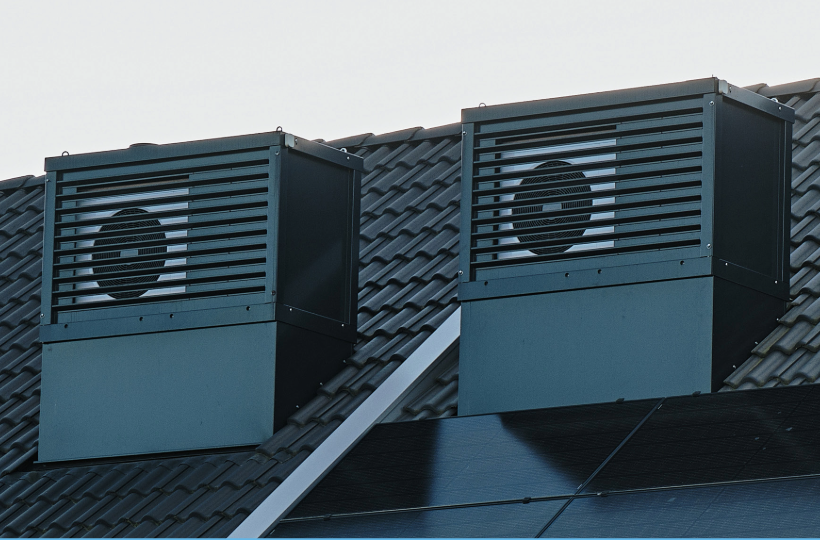 Two heat pumps installed on the side of a house roof. The heat pump have a visible fan. 