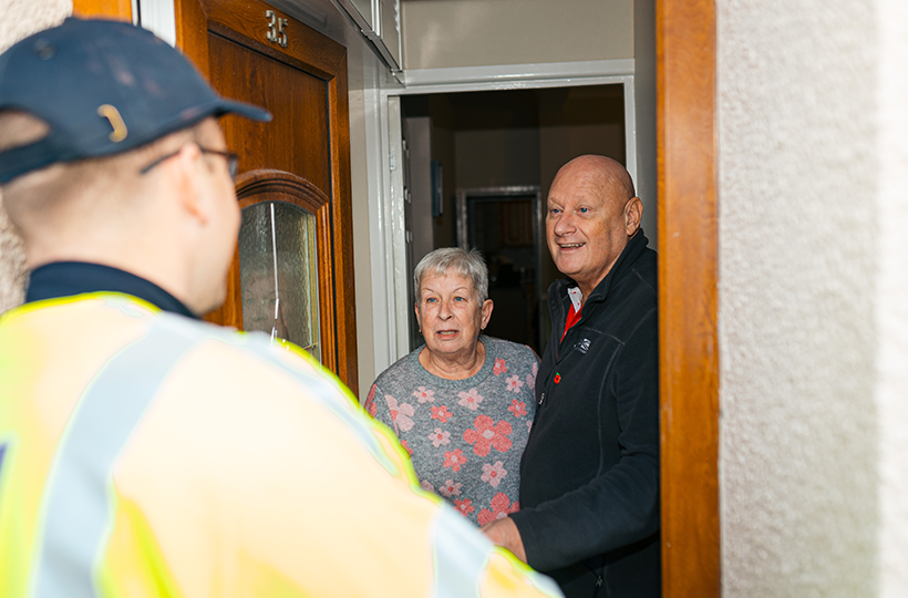 Two older customers chatting to an engineer at their door.