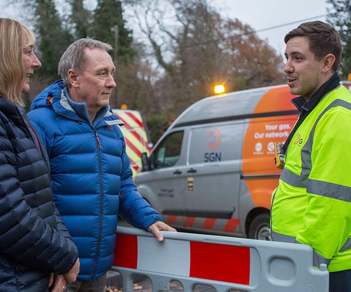 A SGN engineer in high-viz stands near his van talking to two people 