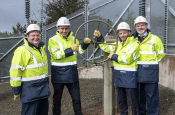 Four men wearing high-vis and hard hats holding a valve to commission a gas pipeline.