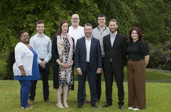 A group of people standing in a field wearing business attire.