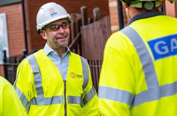 Mark Wild is pictured in a protective jacket and helmet while talking to another engineer who has his back to the camera. Mark is smiling.