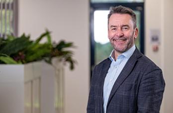 CEO Mark Wild, standing in office wearing shirt and jacket