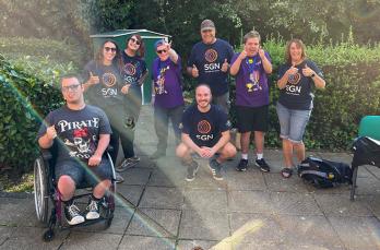 A group of adults in SGN t-shirts with young adults with learning disabilities, all giving thumbs up