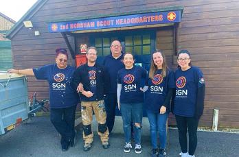 Four women and two men in SGN t-shirts in front of the shed for 2nd Horsham Scouts headquarters