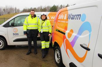 A man and woman in PPE stood in front of two Safe & Warm vans