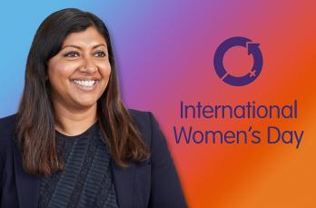 A smiling woman in a business jacket against a gradient with the logo for International Women's Day