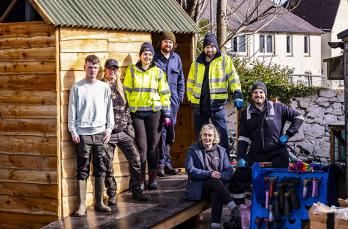 A group of people smiling standing in front of a shed on top of a ramp