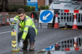 An engineer crouching down on the street using a piece of equipment.