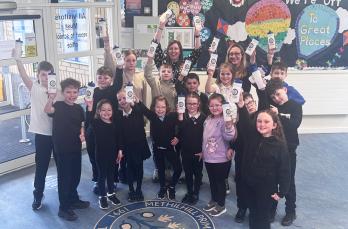A group of school children inside a school holding up plastic water bottles