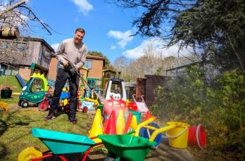 A man powerwashing colourful outdoor plastic toys