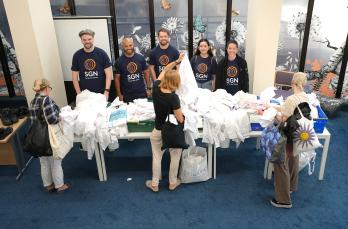 Five SGN volunteers smiling behind a table of school shirts as parents look through them